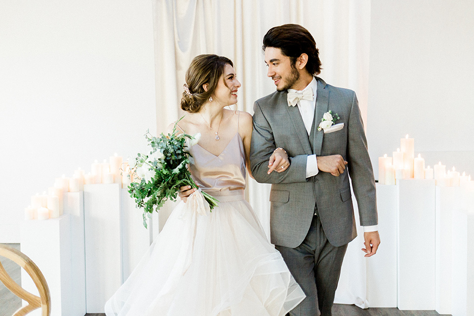 The-1912-Shoot-bride-and-groom-walking-down-aisle-groom-in-a-grey-suit-and-ivory-bow-tie-bride-in-a-tulle-ballgown-with-straps