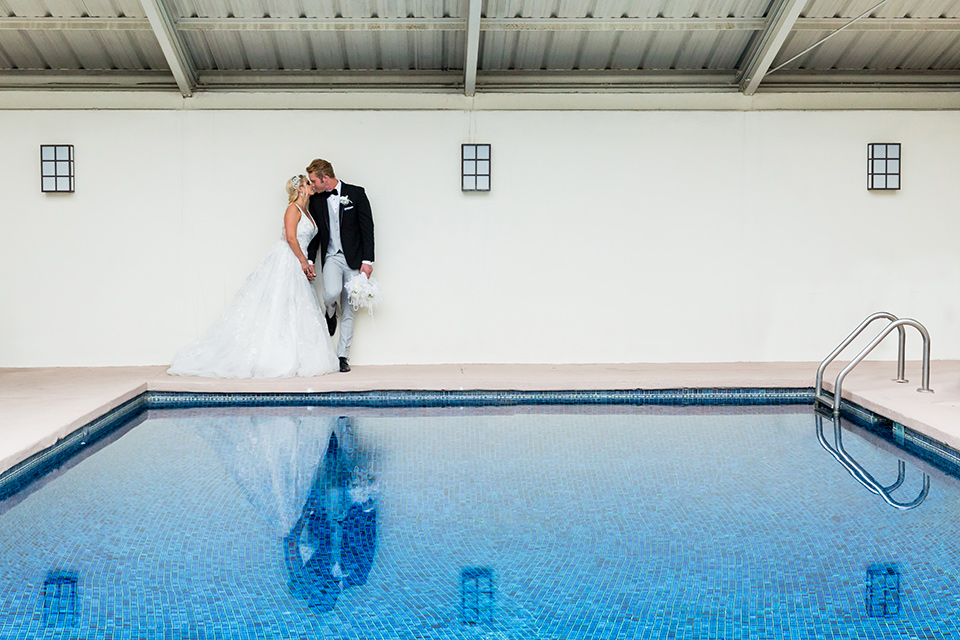 The-Belmar-Hotel-Wedding-bride-and-groom-by-pool-bride-in-a-white-ballgown-with-a-deep-v-neckline-and-hair-in-a-braid-groom-in-a-black-framed-tuxedo=jacket-with-a-light-grey-pant-and-light-grey-vest