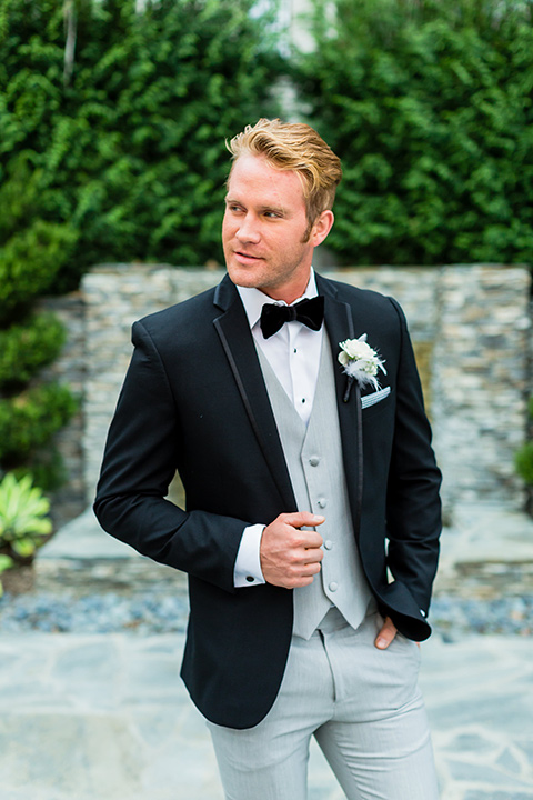 wedding groom standing in a black tuxedo jacket with a light grey vest and pant