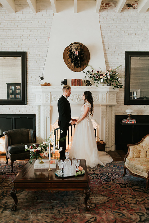 bride in a lace gown with a cap sleeve and illusion neckline and the groom in a black suit with a long black tie inside holding hands