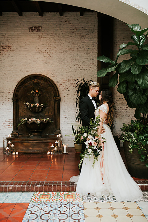 bride in a lace gown with a cap sleeve and the groom in a black suit with a black long tie on tile outside