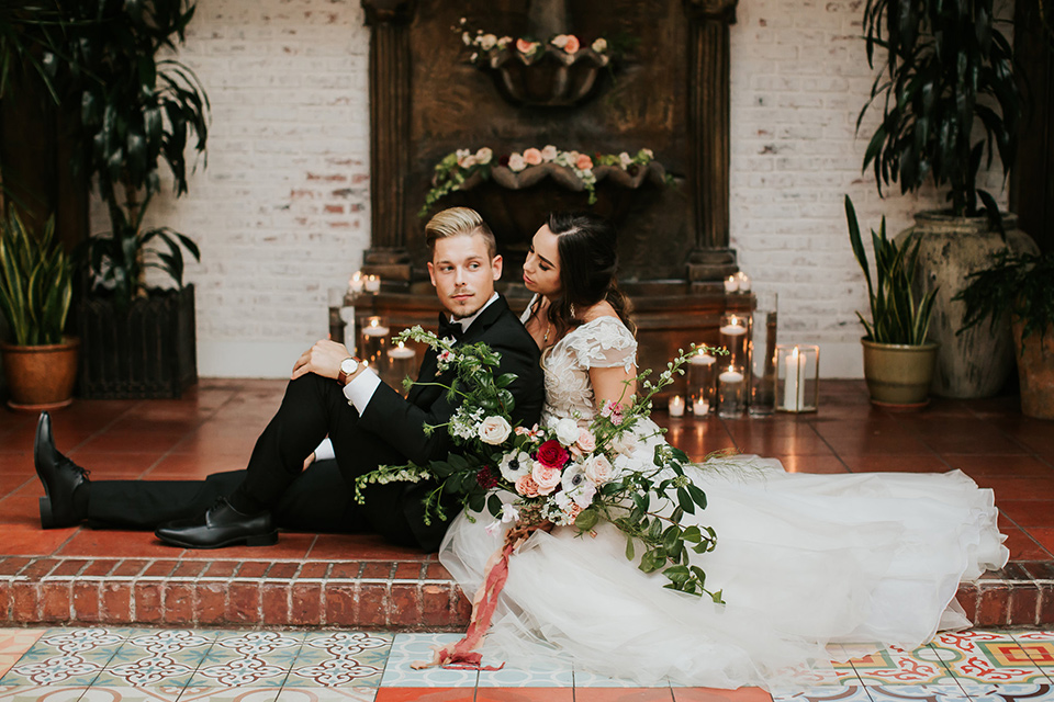 bride in a lace full gown with a cap sleeve and illusion neckline and the groom in a black suit with black long tie sitting on the steps