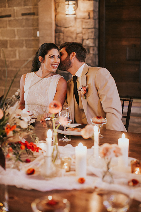 the bride in a white gown with a high neckline and sleeves, along with nude suede heels and her hair in a high ponytail the groom in a tan suit with a chocolate brown long tie