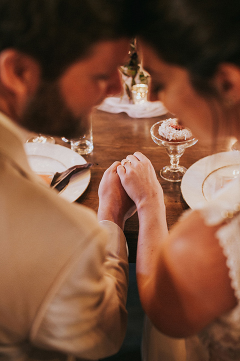  the bride in a white gown with a high neckline and sleeves, along with nude suede heels and her hair in a high ponytail the groom in a tan suit with a chocolate brown long tie 