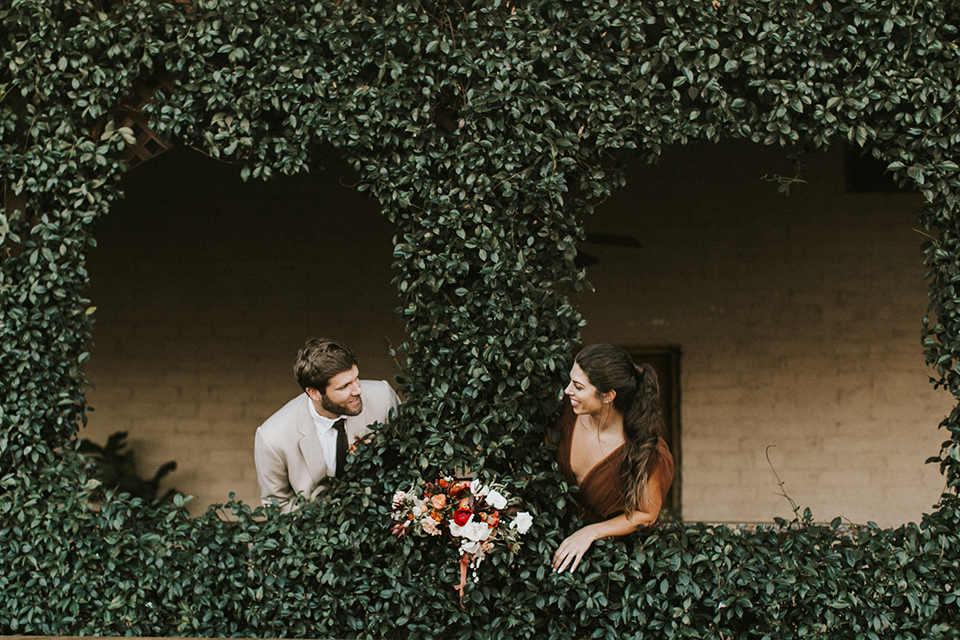  the bride in a chocolate and tan brown gown with a high neckline and sleeves, along with nude suede heels and her hair in a high ponytail and the groom in a tan suit with a chocolate brown long tie