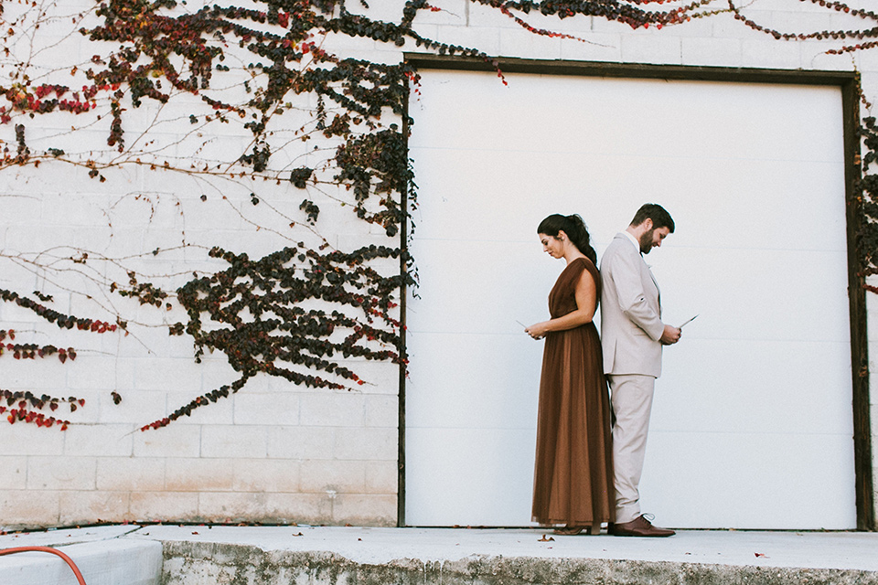  the bride in a chocolate and tan brown gown with a high neckline and sleeves, along with nude suede heels and her hair in a high ponytail and the groom in a tan suit with a chocolate brown long tie