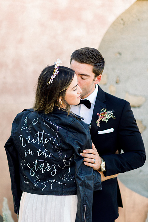 Bride in a cream and ivory flowing gown with a gold headband with stars and a jean jacket and the groom in a black tuxedo with a black bow tie