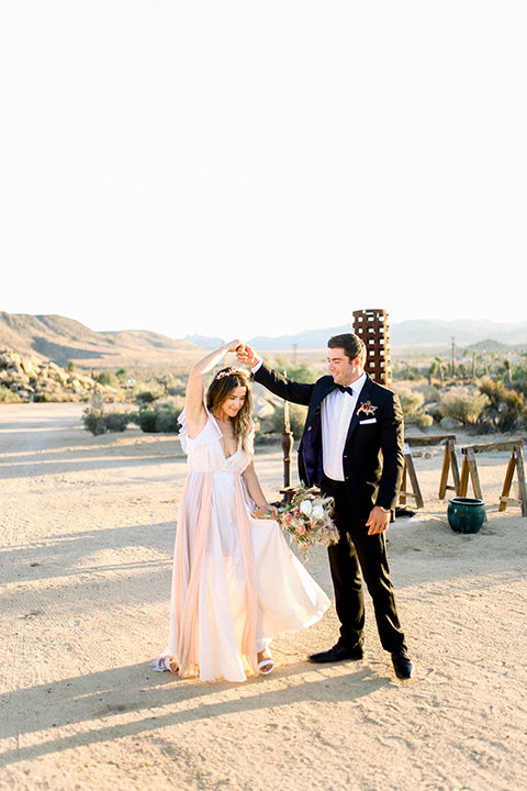 Bride in a cream and ivory flowing gown with a gold headband with stars and the groom in a black tuxedo with a black bow tie dancing