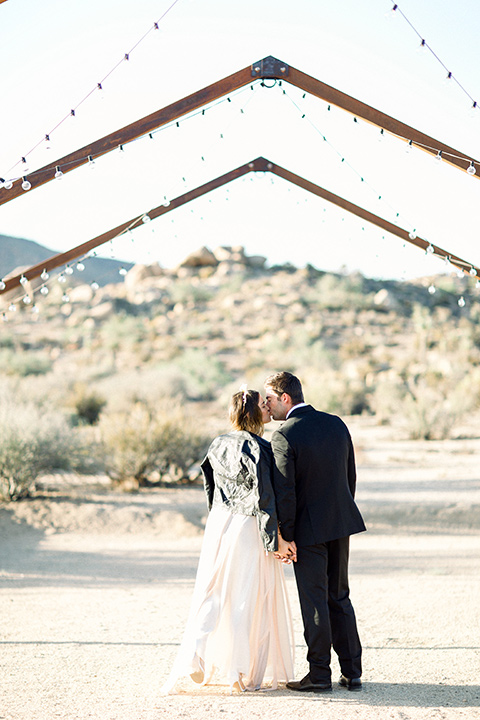 bride in a flowing ivory and rose gold style gown with a gold headband and the groom in a black tuxedo with a black bow tie