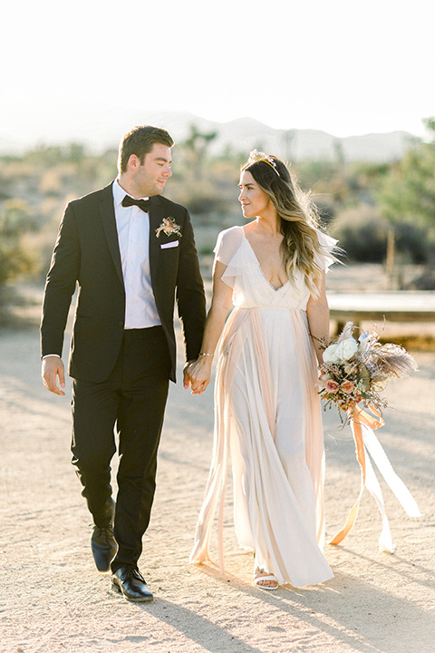 bride in a flowing ivory and rose gold style gown with a gold headband and the groom in a black tuxedo with a black bow tie