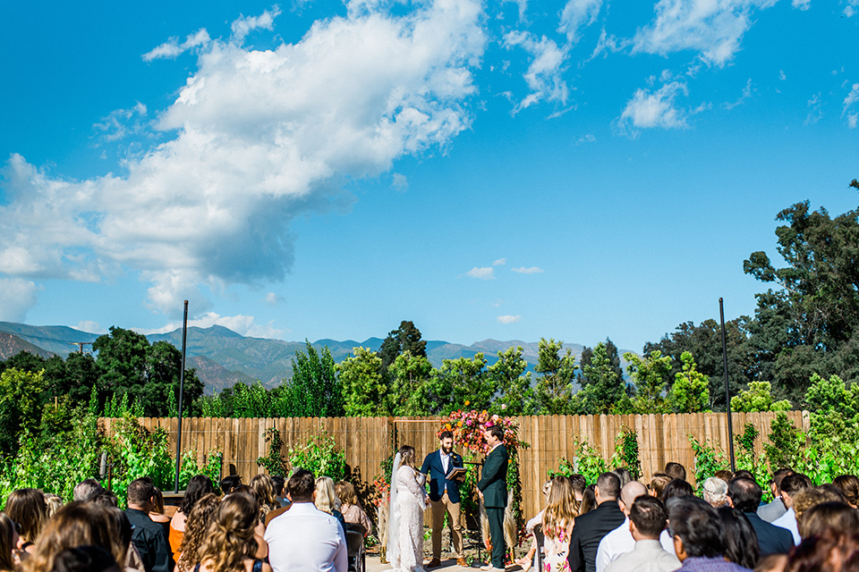 Topa-Winery-Wedding-bride-and-groom-ceremony-bride-in-a-bohemian-lace-gown-with-long-flowing-sleeves-groom-in-a-green-suit-with-a-tan-long-tie