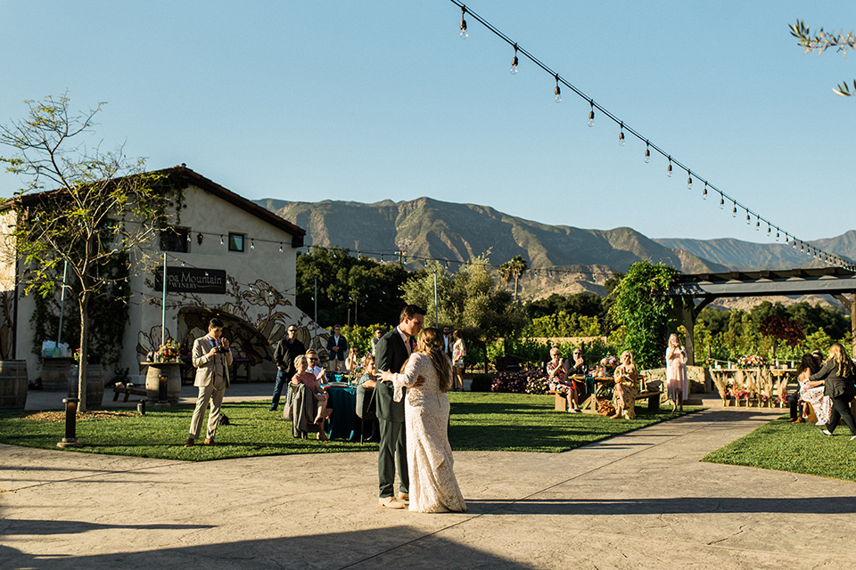 Topa-Winery-Wedding-bride-and-groom-first-dance-bride-in-a-bohemian-lace-gown-with-long-flowing-sleeves-groom-in-a-green-suit-with-a-tan-long-tie