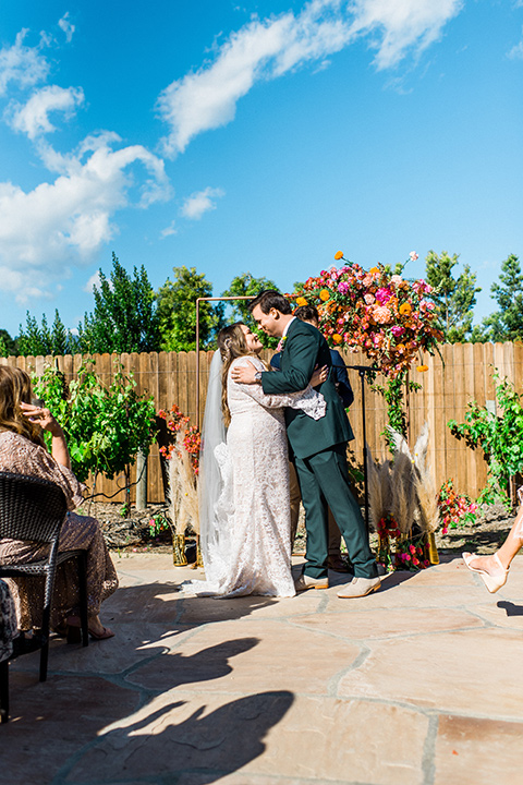 Topa-Winery-Wedding-bride-and-groom-first-kiss-bride-in-a-bohemian-gown-with-lace-detailing-and-flutter-sleeves-groom-in-a-green-suit-with-a-tan-tie-and-shoes