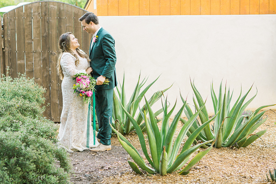 Topa-Winery-Wedding-bride-and-groom-in-venue-garden-bride-in-a-bohemian-lace-gown-with-long-flowing-sleeves-groom-in-a-green-suit-with-a-tan-long-tie