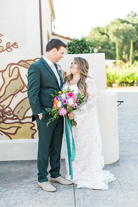 Topa-Winery-Wedding-bride-and-groom-looking-at-each-other-bride-in-a-bohemian-gown-with-lace-detailing-and-flutter-sleeves-groom-in-a-green-suit-with-a-tan-tie-and-shoes