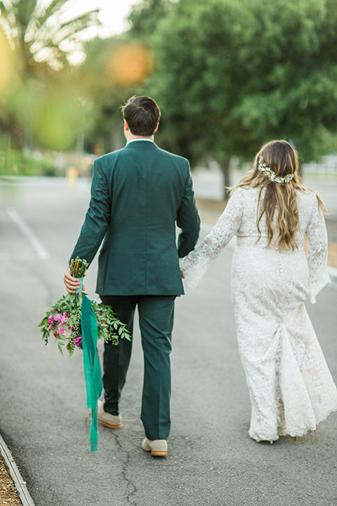 Topa-Winery-Wedding-bride-and-groom-walking-away-from-camera-bride-in-a-lace-bohemian-style-gown-with-flutter-sleeves-groom-in-a-green-suit-with-a-tan-long-tie-with-brown-shoes