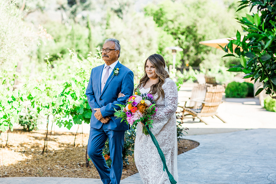 Topa-Winery-Wedding-bride-walking-down-aisle-bride-in-a-bohemian-lace-gown-with-long-flowing-sleeves-father-in-a-light-blue-suit