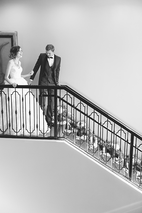 Vellano-Country-Club-black-and-white-photo-of-couple-on-stairs-bride-in-a-big-ballgown-with-her-hair-up-in-a-side-bun-groom-in-a-grey-tuxedo