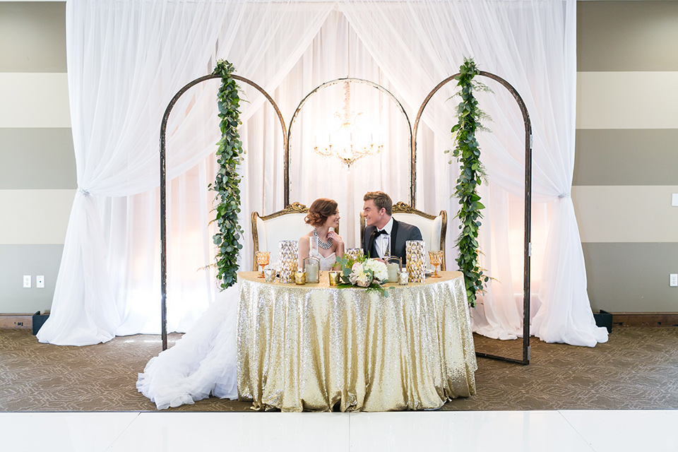 Vellano-Country-Club-bride-and-groom-at-sweetheart-table-bride-in-a-ballgown-with-her-hair-up-groom-in-a-charcoal-grey-tuxedo-with-a-black-bow-tie