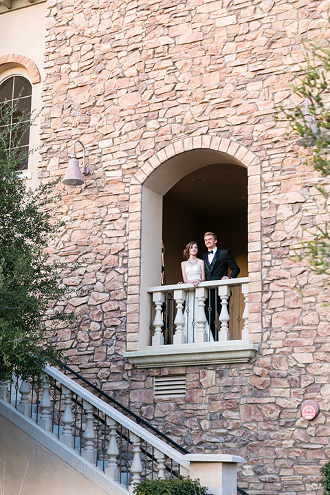 Vellano-Country-Club-bride-and-groom-at-window-bride-in-a-big-ballgown-with-her-hair-up-in-a-side-bun-groom-in-a-grey-tuxedo