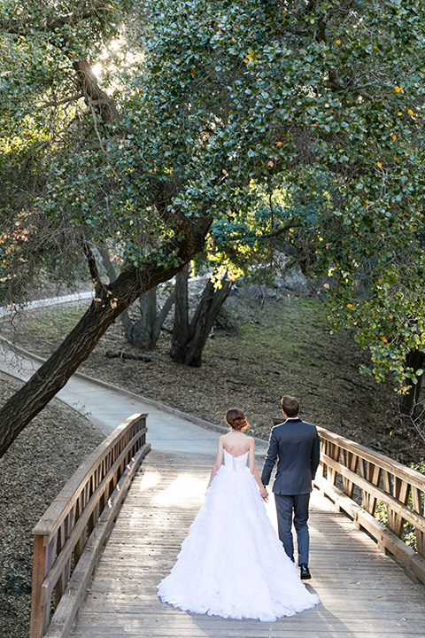 Vellano-Country-Club-bride-and-groom-walking-down-steps-outside-bride-in-a-big-strapless-ballgown-groom-in-a-grey-tuxedo-with-black-bow-tie