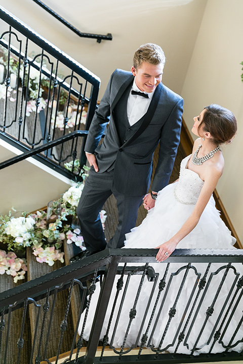 Vellano-Country-Club-bride-and-groom-walking-down-stairs-bride-in-a-big-strapless-ballgown-groom-in-a-grey-tuxedo-with-black-bow-tie