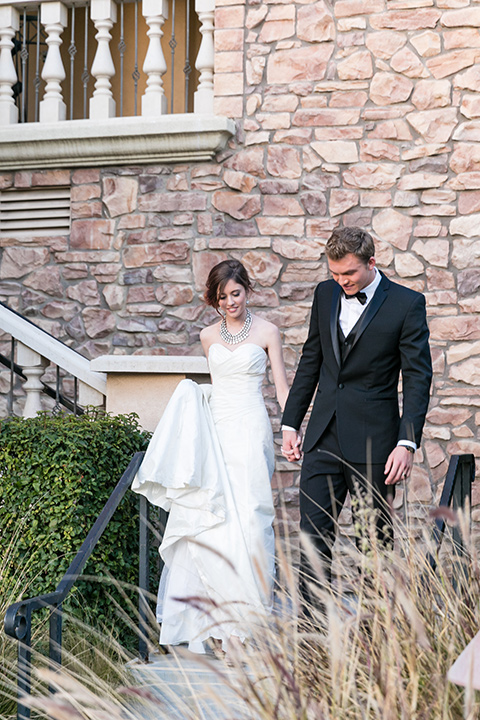 Vellano-Country-Club-bride-and-groom-walking-down-steps-outside-bride-in-a-big-strapless-ballgown-groom-in-a-grey-tuxedo-with-black-bow-tie