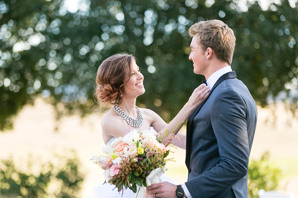 Vellano-Country-Club-bride-fixing-coat-bride-in-a-ballgown-with-her-hair-up-groom-in-a-charcoal-grey-tuxedo-with-a-black-bow-tie