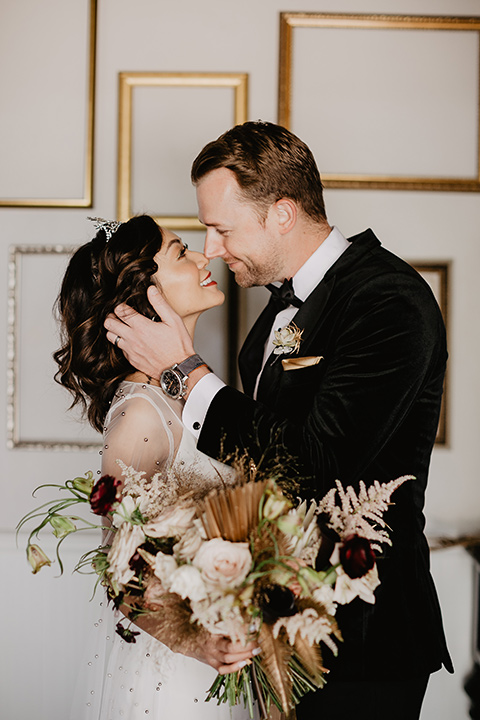 The-Yost-Theatre-bride-and-groom-about-to-kiss-bride-in-a-modern-silk-gown-with-a-sheer-beaded-overlay-groom-in-a-black-velvet-tuxedo