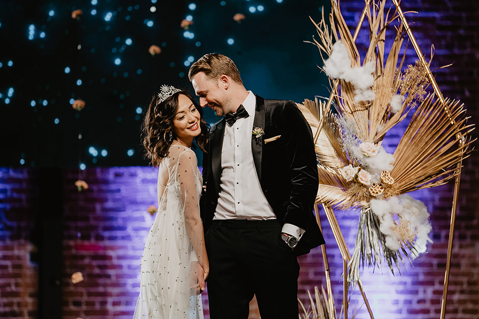 The-Yost-Theatre-bride-and-groom-on-stage-bride-in-a-silk-modern-gown-with-star-accessories-and-groom-in-a-velvet-black-tuxedo