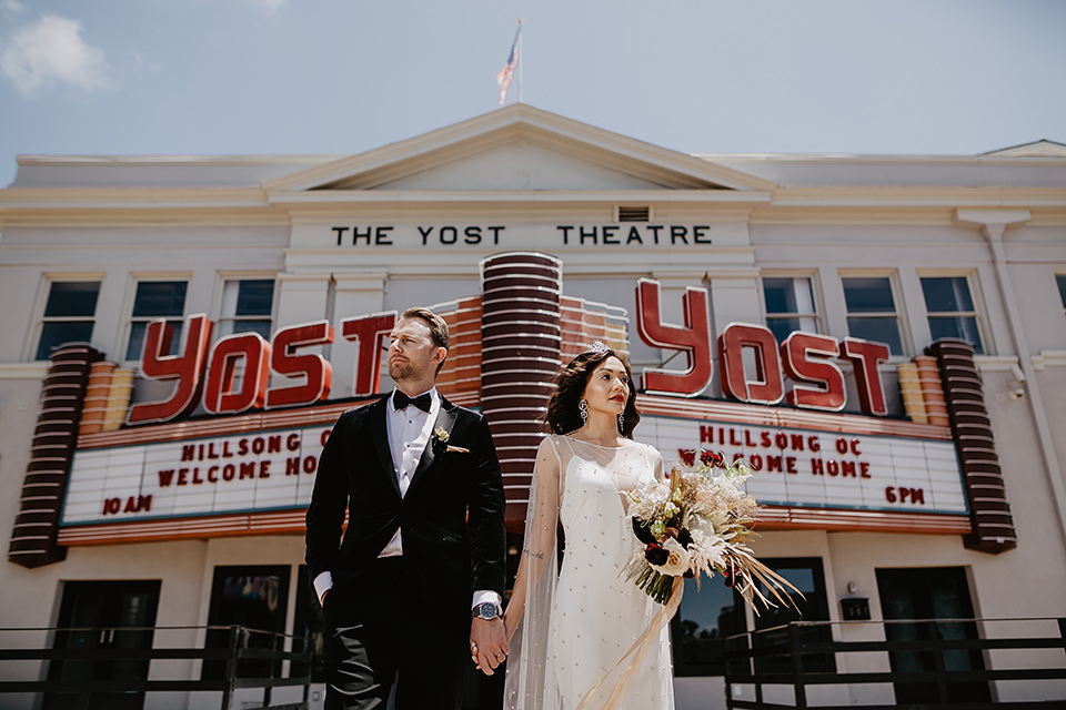 The-Yost-Theatre-bride-and-groom-outside-venue-looking-away-from-each-other-bride-in-a-silk-modern-gown-with-star-accessories-and-groom-in-a-velvet-black-tuxedo