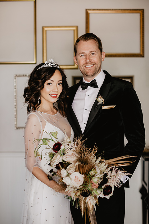 The-Yost-Theatre-bride-and-groom-smiling-at-camera-bride-in-a-modern-gown-with-jeweled-detailing-groom-in-a-velvet-tuxedo