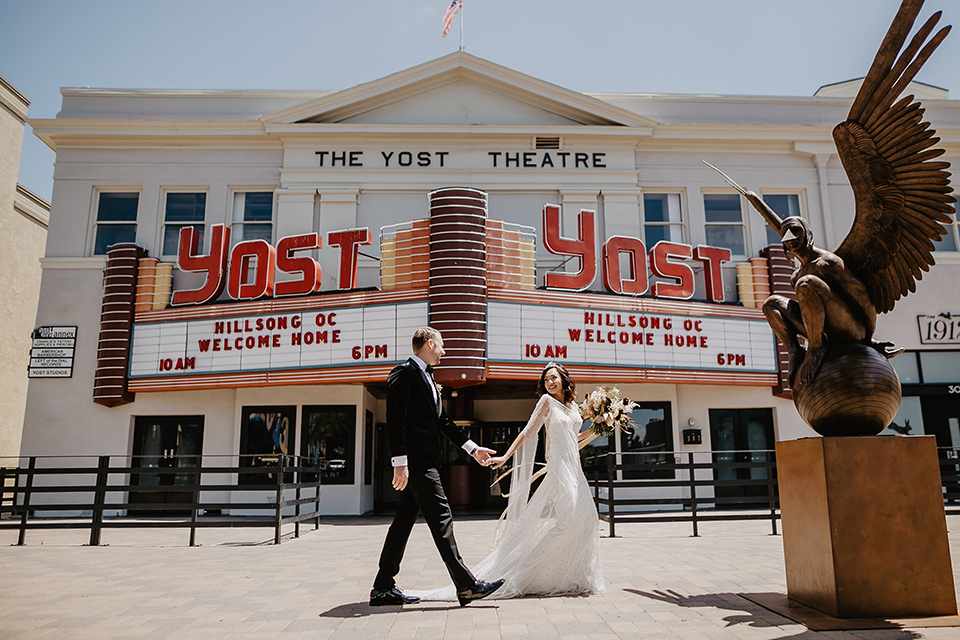 The-Yost-Theatre-bride-and-groom-walking-past-venue-bride-in-a-silk-modern-gown-with-star-accessories-and-groom-in-a-velvet-black-tuxedo