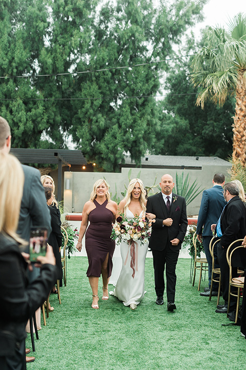 the-lautner-compound-wedding-bride-walking-down-aisle-bride-in-a-lace-formfitting-gown-groom-in-a-navy-shawl-lapel-tuxedo