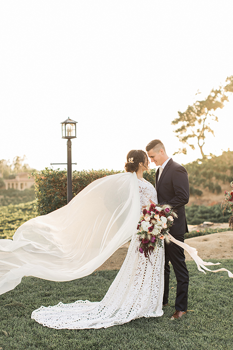 Temecula-outdoor-wedding-at-callaway-winery-bride-and-groom-hugging-and-smiling-bride-in-a-lace-gown-and-groom-in-a-black-notch-lapel-suit