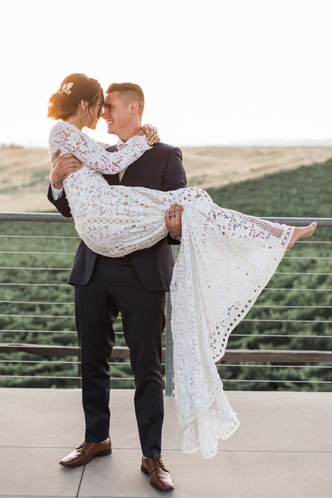 Temecula-outdoor-wedding-at-callaway-winery-bride-and-groom-hugging-carrying-bride-bride-in-a-lace-gown-and-groom-in-a-blue-notch-lapel-suit
