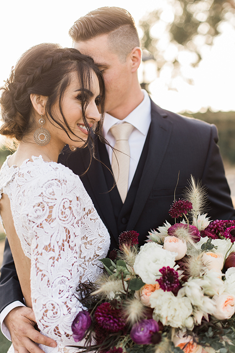 Temecula-outdoor-wedding-at-callaway-winery-bride-and-groom-hugging-close-up-bride-in-a-lace-gown-and-groom-in-a-navy-notch-lapel-suit