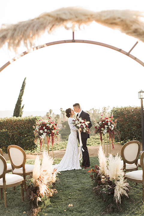 Temecula-outdoor-wedding-at-callaway-winery-ceremony-bride-and-groom-standing-kissing-bride-in-a-lace-dress-with-sleeves-groom-in-a-dark-blue-notch-lapel-suit