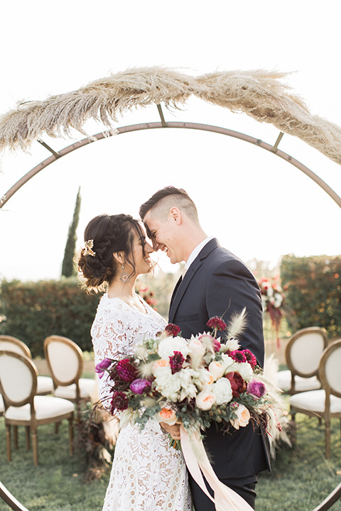 Temecula-outdoor-wedding-at-callaway-winery-ceremony-bride-and-groom-standing-bride-in-a-lace-bohemian-dress-groom-in-a-navy-suit