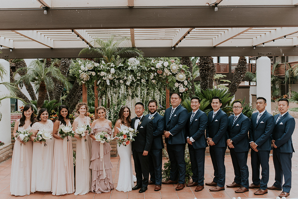 la-jola-shores-hotel-wedding-bridal-party-in-a-line-bridesmaids-in-pink-dresses-groomsmen-in-dark-blue-suits-bride-in-a-formfitting-satin-dress-with-straps-groom-in-a-navy-tuxedo-with-black-shawl-lapel