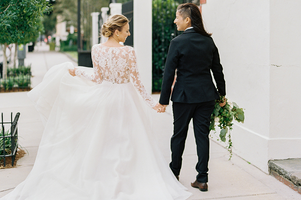 flower-market-shoot-brides-walking-away-from-camera-one-in-a-full-ball-gown-the-other-in-a-black-tuxedo