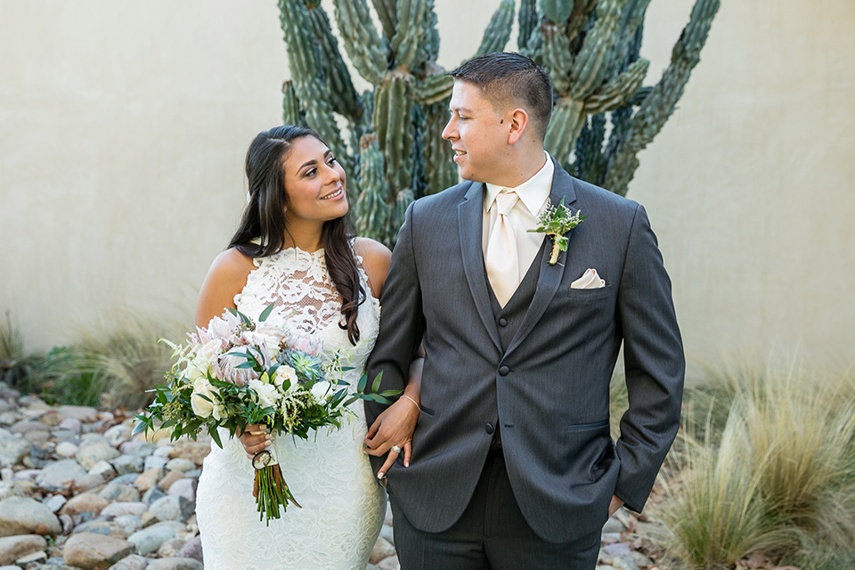 gallway-downs-wedding-bride-and-groom-by-cactus-smiling-at-each-other-bride-in-a-lace-form-fitting-gown-with-a-high-neckline-and-keyhole-back-groom-in-a-charcoal-tux-withan-ivory-long-tie