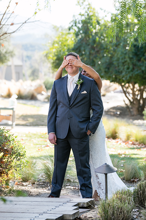 gallway-downs-wedding-bride-covering-grooms-eyes-bride-in-a-lace-formfitting-dress-with-a-high-neckline-and-keyhole-back-groom-in-a-charcoal-tuxxedo-with-nude-long-tie