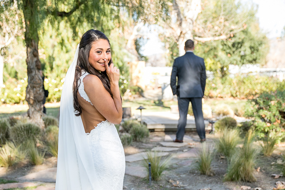 gallway-downs-wedding-bride-telling-camera-to-be-quiet-before-the-first-look-bride-in-a-lace-form-fitting-gown-with-a-high-neckline-and-keyhole-back-groom-in-a-charcoal-tux-withan-ivory-long-tie