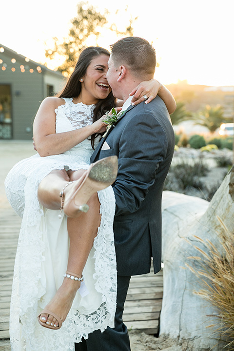 gallway-downs-wedding-groom-holding-bride-bride-in-a-lace-dress-with-a-high-slit-and-a-high-neckline-groom-in-a-dark-grey-suit