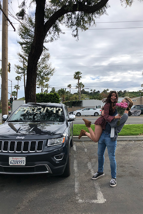 boy holding up girl after putting post-it notes spells out prom on her car