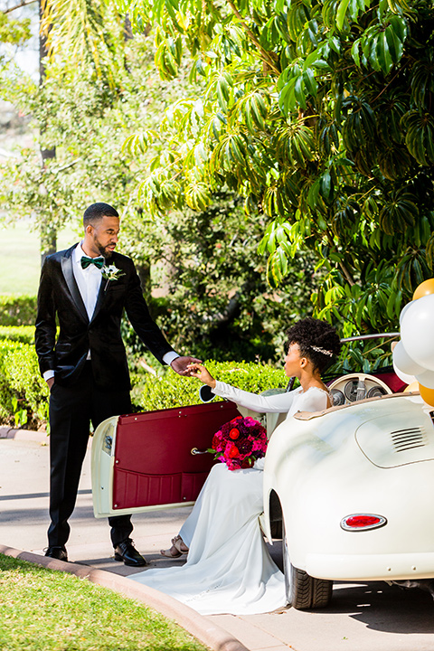 muckenthaler-mansion-groom-helping-bride-out-of-car-bride-in-a-satin-white-gown-and-long-sleeves-and-groom-in-a-black-velvet-tuxedo-and-green-velvet-bow-tie