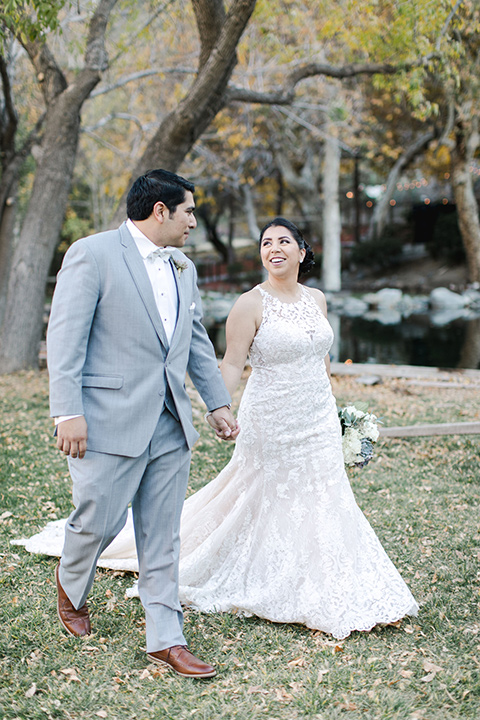 hidden-acres-wedding-bride-and-groom-walking-bride-in-a-fitted-lace-gown-with-groom-in-grey-suit-with-white-bow-tie