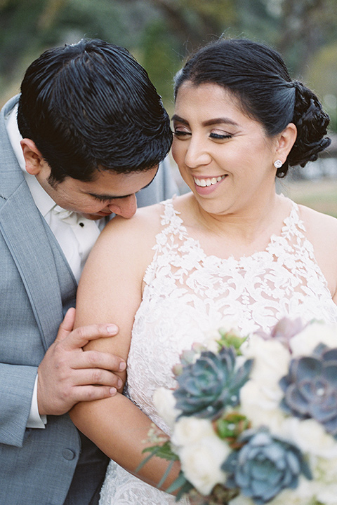 hidden-acres-wedding-close-up-of-ciuple-groom-kissing-her-shoulder-bride-in-fitted-gown-with-lace-detailing-groom-in-light-grey-suit