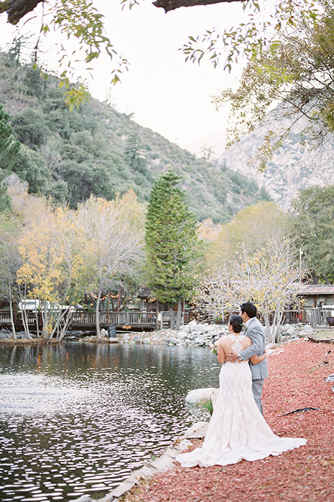 hidden-acres-wedding-couple-bu-lake-bride-in-fitted-gown-with-lace-detailing-groom-in-light-grey-suit